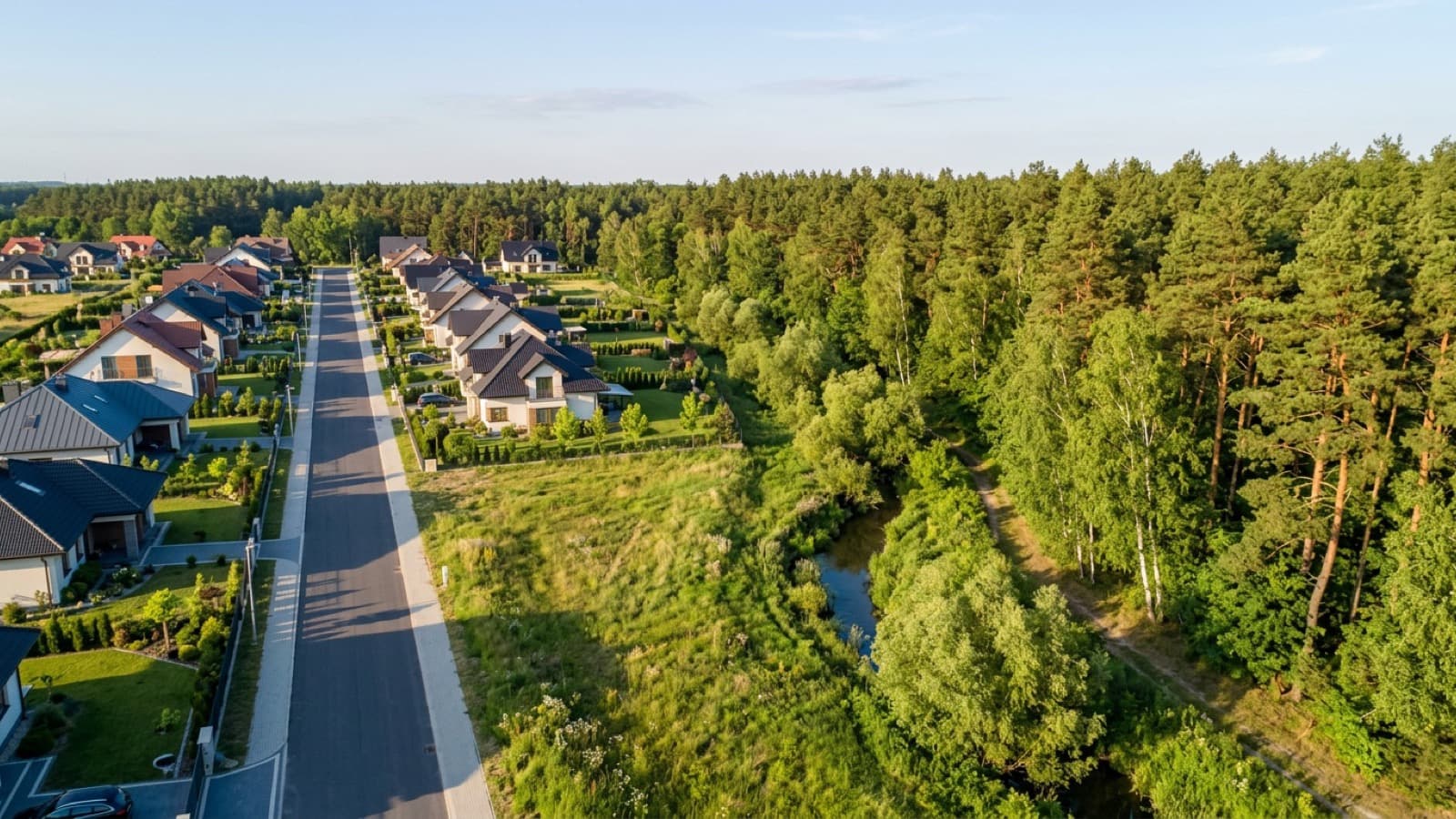 Ostatni rząd domów na skraju osiedla, pusta działka, strumień i las tuż za nią